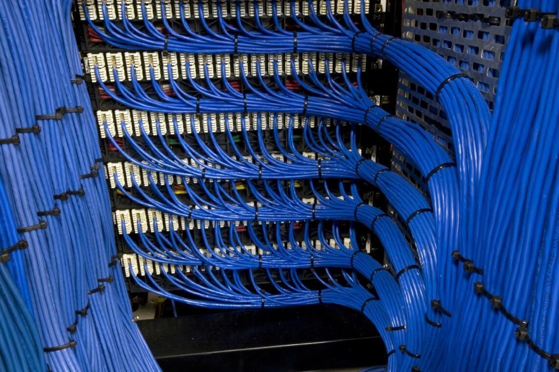 Electrician installing structured CAT6 data cabling in a London office network cabinet