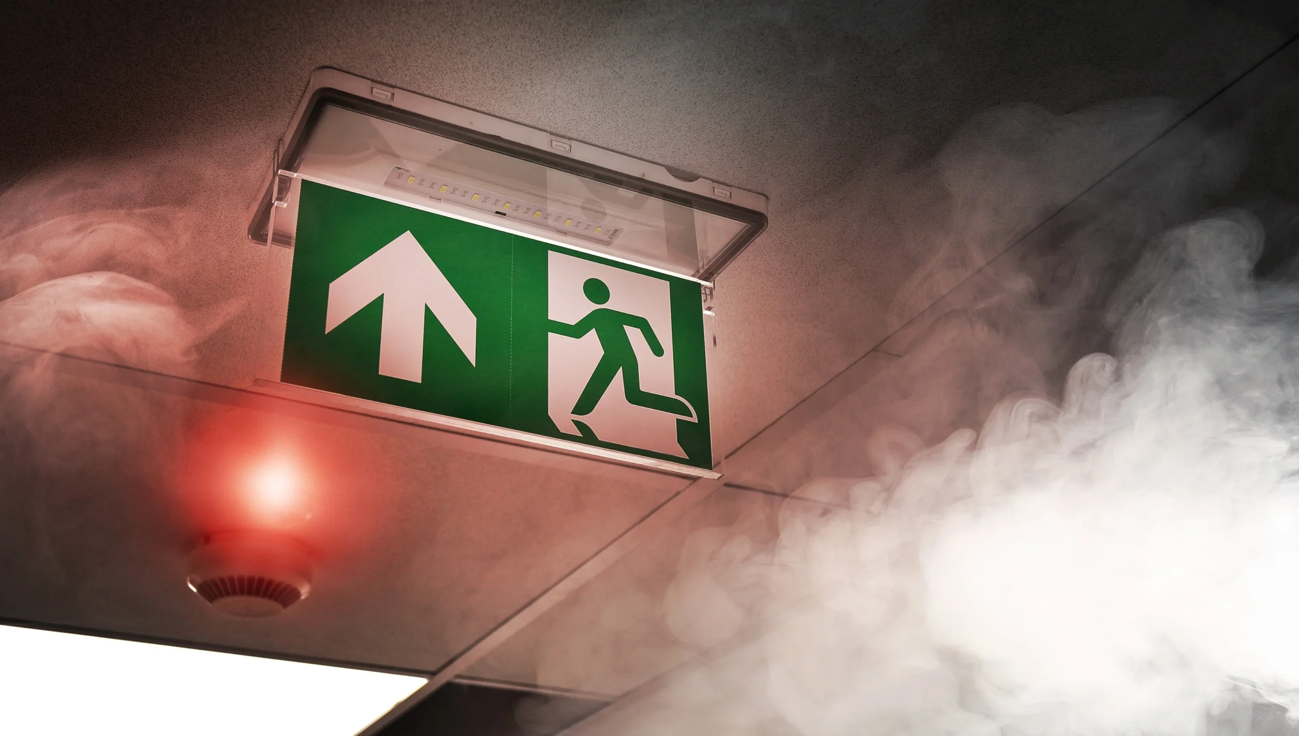 Electrician installing commercial fire alarm panel and emergency lighting in a London office corridor